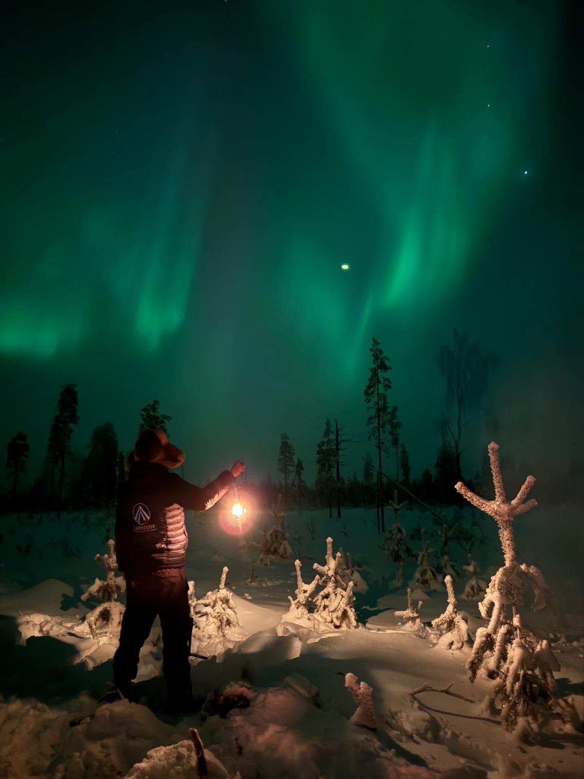 A guy holding a lantern under the northern lights